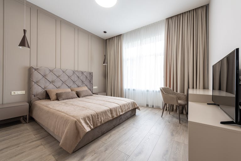 A spacious modern bedroom featuring neutral decor, plush bedding, and elegant lighting.