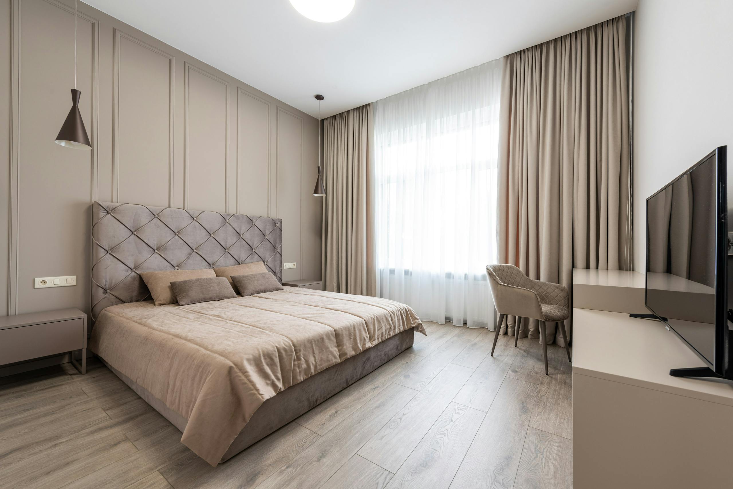 A spacious modern bedroom featuring neutral decor, plush bedding, and elegant lighting.